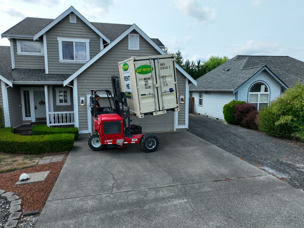 A red Moffett places a 6 foot EZ Move container in a customer's driveway.